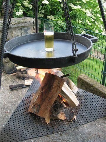 Ein Feuerplatz mit einem großen, hängenden Topf über einem offenen Feuer. Neben dem Topf steht ein Glas Bier.