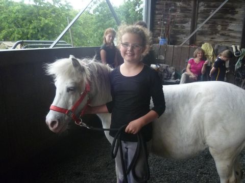 Op de voorgrond van de afbeelding staat een meisje in een zwart T-shirt en een grijze broek voor een wit Pony. In haar linkerhand houdt ze een zwart touw, met haar rechterhand krabt ze het Pony onder het hoofd. Het Pony draagt een rood hoofdstel.
Op de achtergrond zijn nog enkele personen te zien. Ze bevinden zich in een stallen.