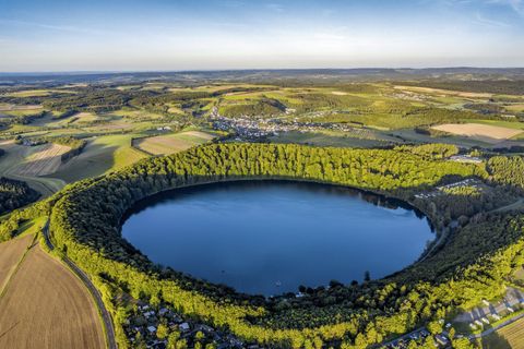 Ein schöner Kratersee, umgeben von grünen Wäldern und landwirtschaftlichen Feldern. Die Landschaft strahlt Ruhe und Naturverbundenheit aus.