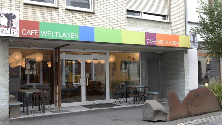 Das Bild zeigt das Café Weltladen mit einer bunten Fassade. Es gibt Tische und Stühle im Freien, die zum Verweilen einladen.