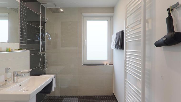 Een moderne badkamer met een douche van glas en een witte wastafel. De ruimte is licht en minimalistisch ingericht.