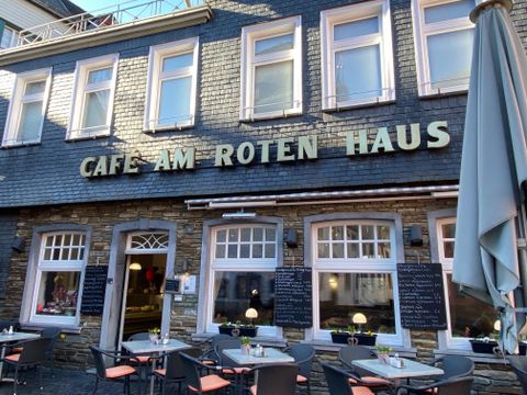 Ein gemütliches Café mit dem Namen „Cafe am Roten Haus“. Es gibt Tische im Freien und eine einladende Atmosphäre.