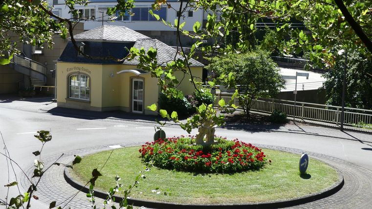 Ein schöner Kreisverkehr mit bunten Blumenbeeten und einer kleinen Pavillon. Umgeben von Bäumen und einem ruhigen Wohnviertel.