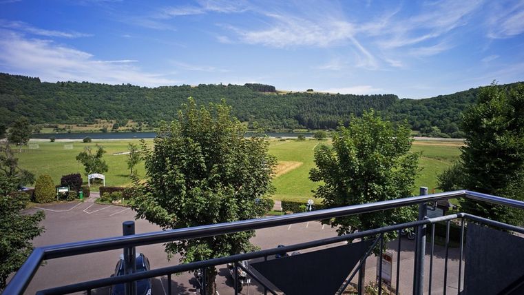 A beautiful view from a balcony onto a green landscape with trees. In the background, gentle hills and a blue sky can be seen.
