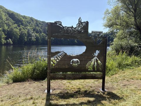 Eine kunstvolle Schnitzerei zeigt eine Landschaft mit einem Fluss und Bergen. Im Hintergrund sind Bäume und eine alte Burg sichtbar.