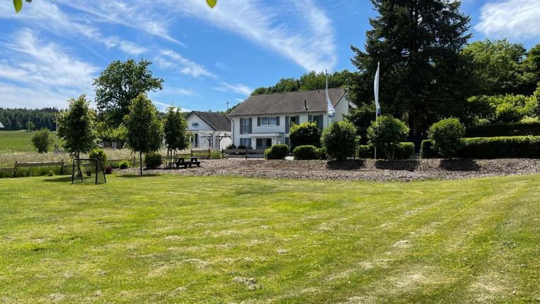 A beautiful property with a large, green garden. In the background, you can see a modern house surrounded by trees and bushes.