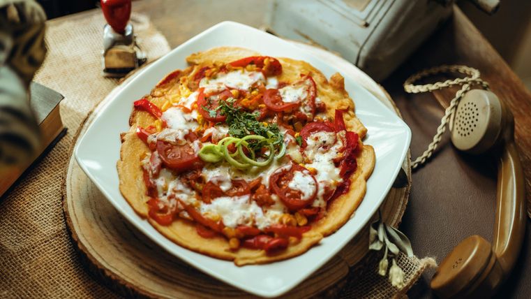 A delicious pizza plate with fresh vegetables and cheese. Vintage objects are visible in the background.
