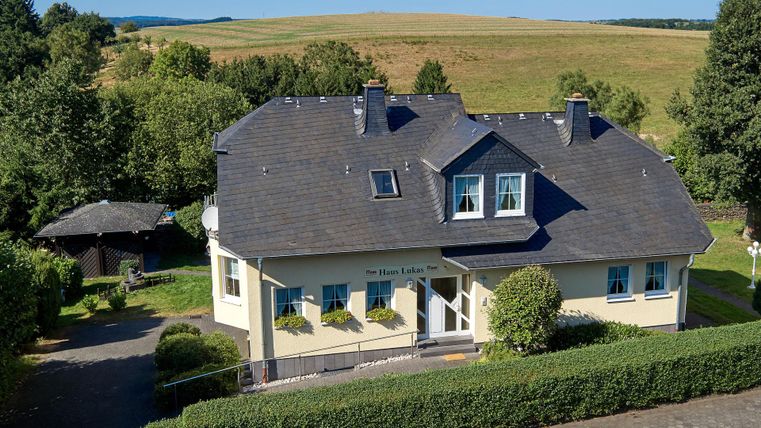 Een modern huis met een mooi aangelegde tuin. Op de achtergrond zijn groene velden en een heldere lucht te zien.