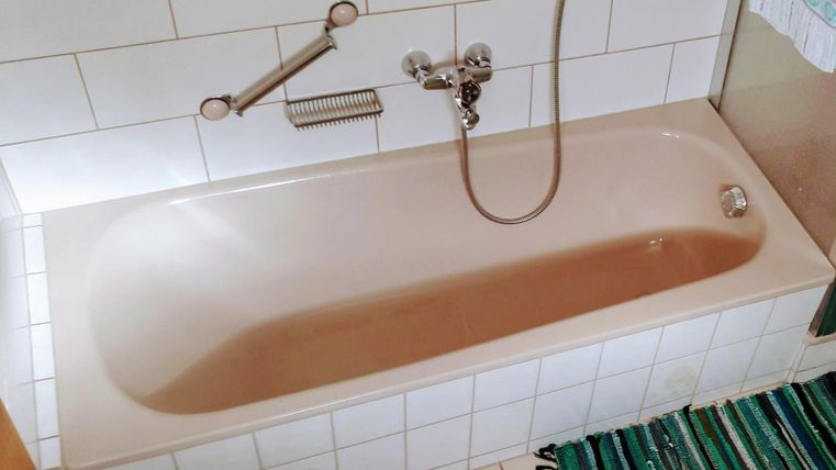 Een eenvoudig bad op witte tegels. Ernaast ligt een gestreepte tapijt.