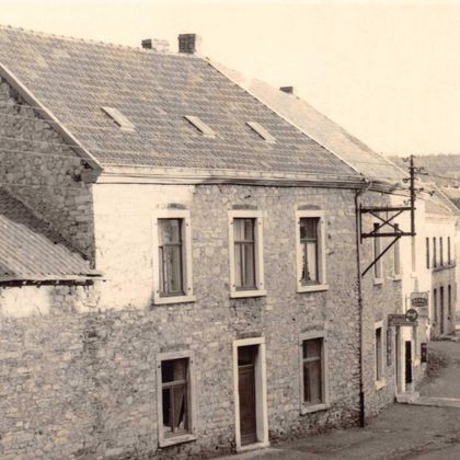 Een oud, stenen huis aan een rustige straat. Op de achtergrond zijn meerdere andere gebouwen en bomen zichtbaar.