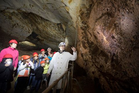 Eine Gruppe von Menschen mit Helmen steht in einer Höhle. Ein Führer erklärt die Felsformationen im Hintergrund.