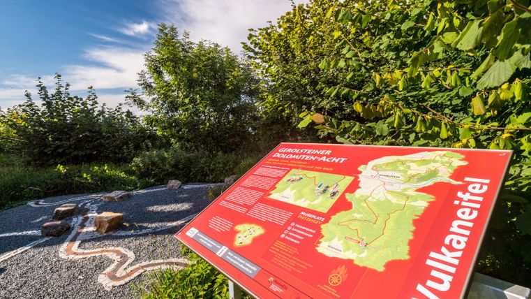 Informationsschild am Mußeplatz an der Dietzenley im Keltenpfad, umgeben von Bäumen und einem klaren Himmel.