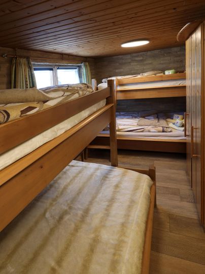 A cozy sleeping area with wooden bunk beds. The room has a warm atmosphere due to the wooden paneling and natural light.