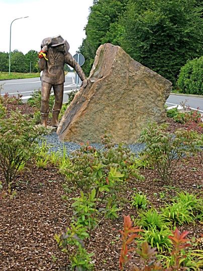 Een standbeeld van een duiker die met een grote steen interactie heeft. Omringd door kleurrijke planten.