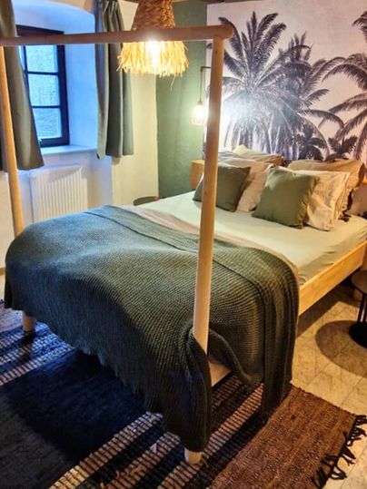 A modern bedroom with a double bed and a cozy rug. The walls are decorated with palm motifs, and there are stylish windows with curtains.