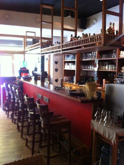 Eine gemütliche Bar mit Holzregalen und einer langen Theke. Gläser und Getränke sind ordentlich aufgestellt.