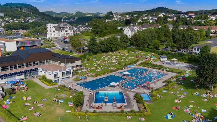 Luftaufnahme des Freibads Gerolstein mit Schwimmbecken, Liegewiese und umliegender Landschaft.