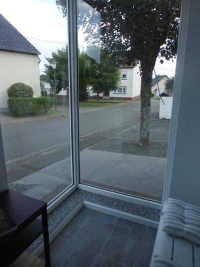 Ein heller Eingangsbereich mit großen Fenstern. Draußen ist eine ruhige Straße und ein Baum sichtbar.