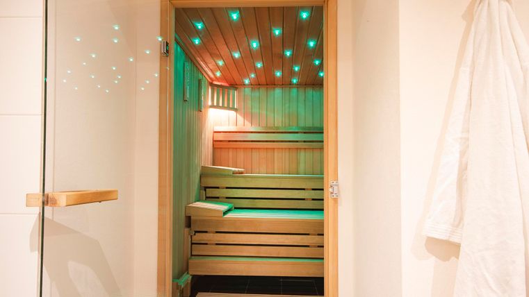 A modern sauna with wooden shelves and atmospheric lighting. The glass door offers a view of the warm interior.
