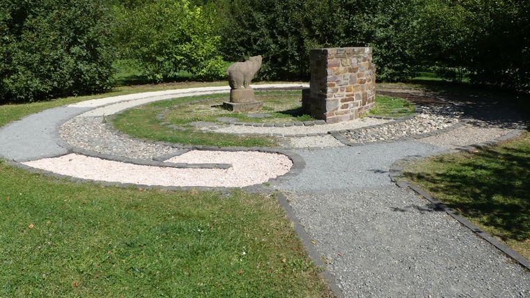 Ein stilvoller Garten mit einem spiralförmigen Weg aus Kies und Stein. In der Mitte steht ein quadratischer Steinblock als Blickfang.