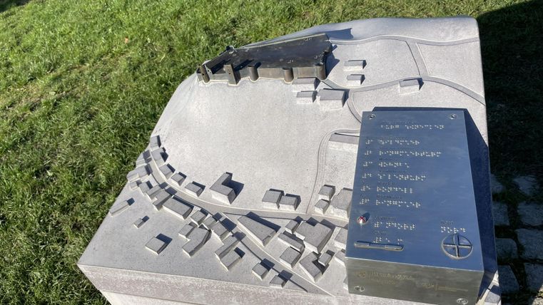 Ein detailliertes Modell einer Stadt auf einem Informationsstele. Es zeigt Gebäude und Straßen im Relief mit einer Beschriftung.