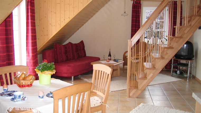 Ein gemütliches Wohnzimmer mit rotem Sofa und einem Esstisch. Die Treppe führt zu einem anderen Stockwerk, und das Raumdesign strahlt Wärme aus.