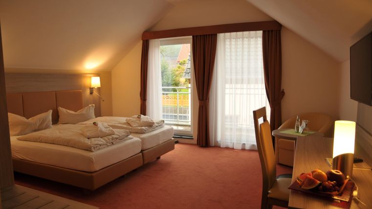 Ein gemütliches Hotelzimmer mit zwei Betten und einem Schreibtisch. Große Fenster sorgen für viel Tageslicht und einen Blick nach draußen.