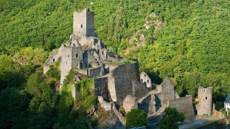 An old castle ruin in the greenery, surrounded by forest. The structure is partly collapsed, but impressive in the landscape.
