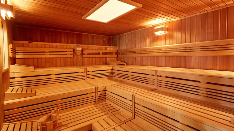 Interior view of an empty wooden sauna with benches and a bucket.