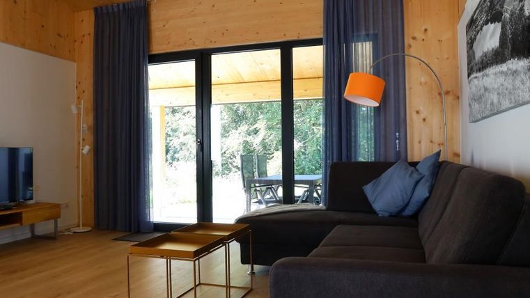 Ein modernes Wohnzimmer mit einem großen Sofa und einem Couchtisch. Große Fenster bieten einen Blick auf die grüne Terrasse.