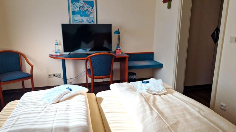 A simple hotel room with two separate beds. A table with a television and chairs is also available.