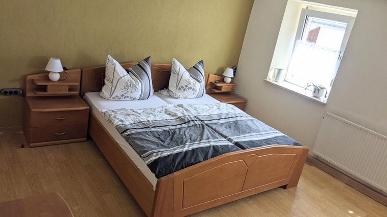 A cozy bedroom with a double bed and two nightstands. The room has a bright wall and a window that lets in daylight.