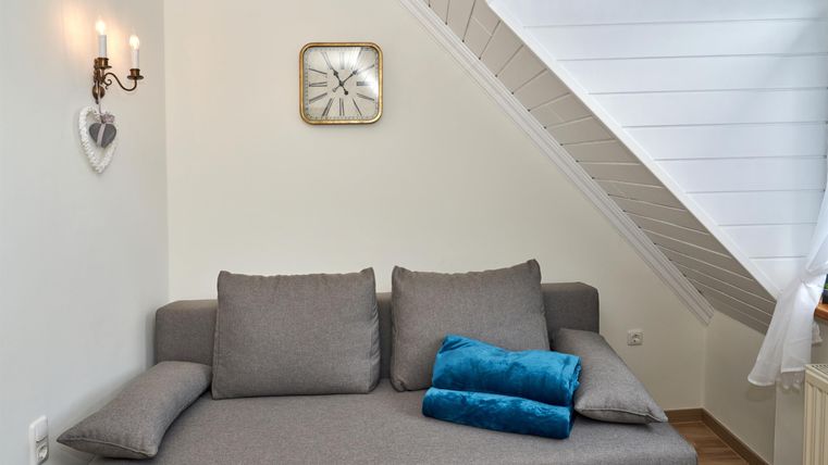 A cozy living room with a gray sofa and blue cushions. On the wall hangs a clock and there is soft lighting.