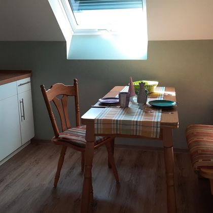 A cozy kitchen with a small dining area. The table is set and the light falls through a window onto the furniture.