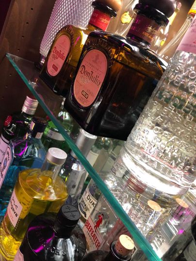 Eine Auswahl an verschiedenen Spirituosen auf einem Regal. Die Flaschen sind in unterschiedlichen Farben und Formen angeordnet.