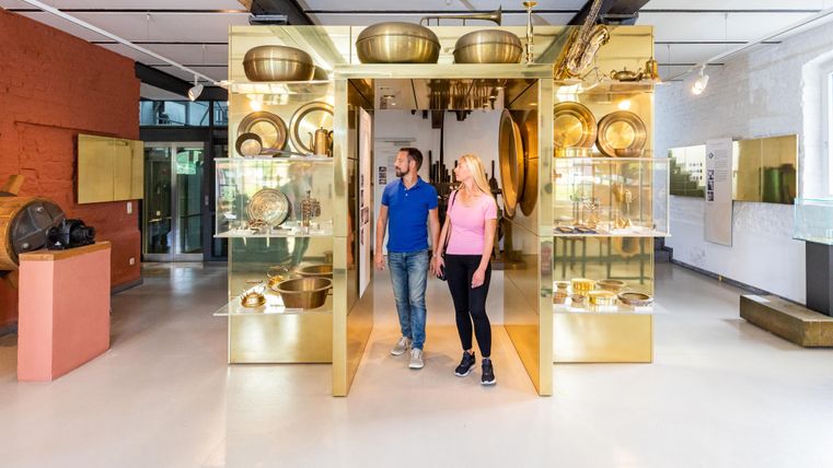 A modern museum with shiny display cases showcasing various objects. Two people are curiously exploring the exhibitions.