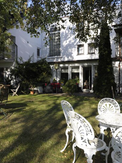 Ein schönes Haus mit einem gepflegten Garten. Im Vordergrund steht ein eleganter Tisch mit Stühlen aus Weißmetall.