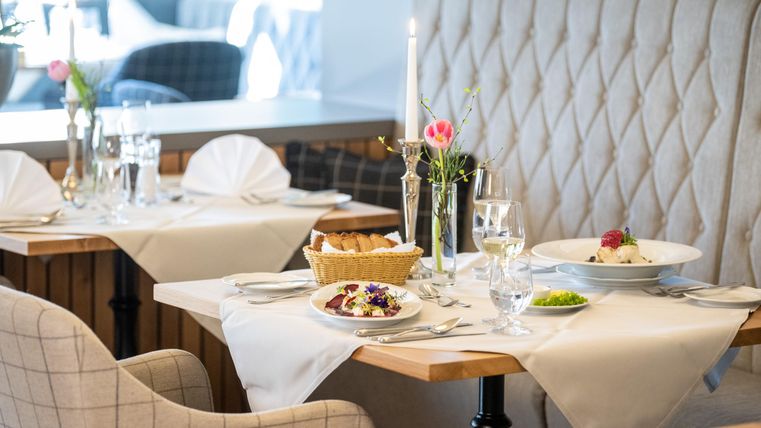 Ein elegantes Restaurant mit schön gedeckten Tischen. Auf den Tischen stehen frische Blumen, Besteck und kunstvoll angerichtete Gerichte.