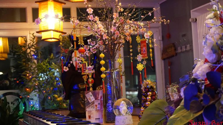 Eine gemütliche Restaurantatmosphäre mit dekorativen Laternen und einem Blumenarrangement. Der Tisch ist mit verschiedenen japanischen Gegenständen und Pflanzen geschmückt.