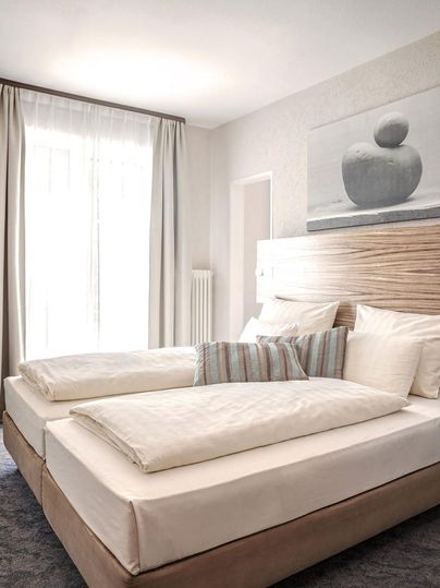 Een heldere en moderne slaapkamer met twee eenpersoonsbedden. De inrichting is eenvoudig en elegant, met een raam dat veel daglicht binnenlaat.