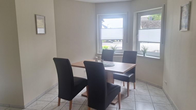 Ein heller Essbereich mit einem Tisch und vier Stühlen. Das Zimmer hat große Fenster, die für viel Tageslicht sorgen.