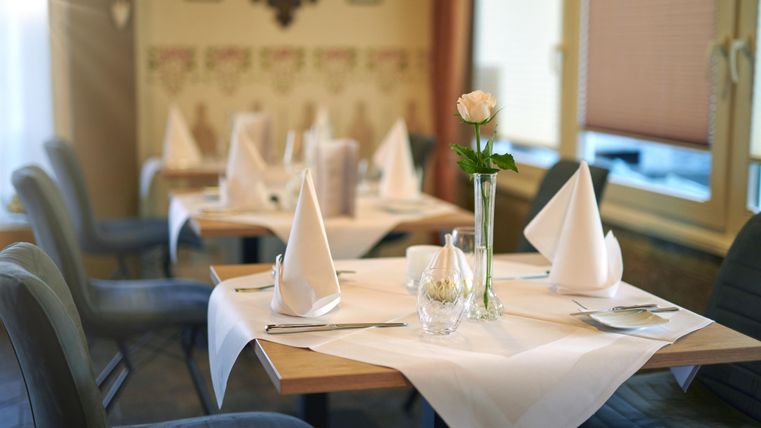 An elegantly decorated table in a restaurant with white tablecloths and fabric napkins. A single rose in a vase complements the stylish atmosphere.