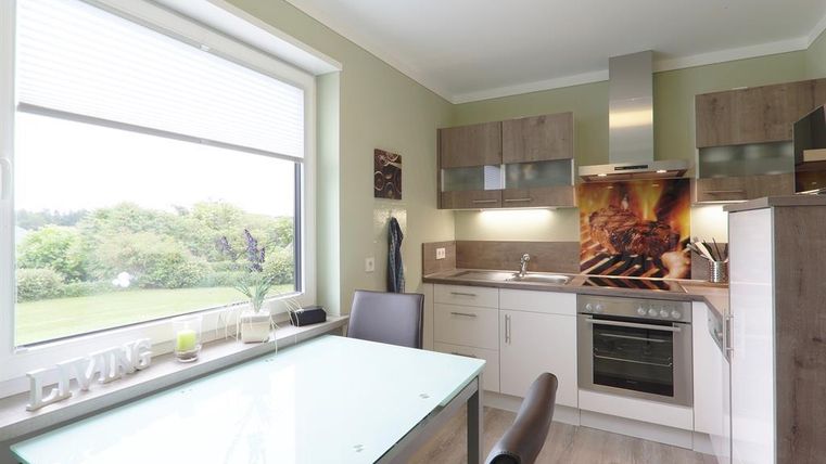 Een moderne keuken met een eetgedeelte en grote ramen. Lichtgroene muren en houten kasten creëren een uitnodigende sfeer.