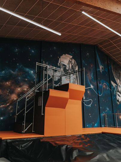 Eine Sprungfläche mit orangefarbenem Podest und einem Raumfahrthintergrund. Die Wände sind mit einer Weltraumgrafik dekoriert.