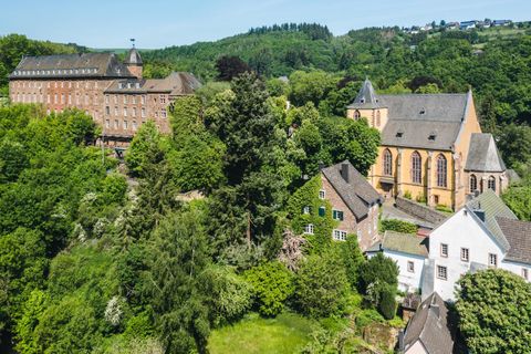 Een schilderachtig dorp met historische gebouwen en weelderig groen. Op de achtergrond zijn bomen en zachte heuvels te zien.
