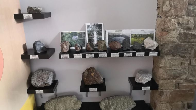 Eine Vitrine mit verschiedenen Gesteinsproben und Bildern von Landschaften. Die Stücke sind auf Regalen ausgestellt und beschriftet.