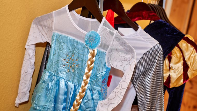 Costumes for children are hanging on a hanger. Below is a charming blue dress with a long braid wig.