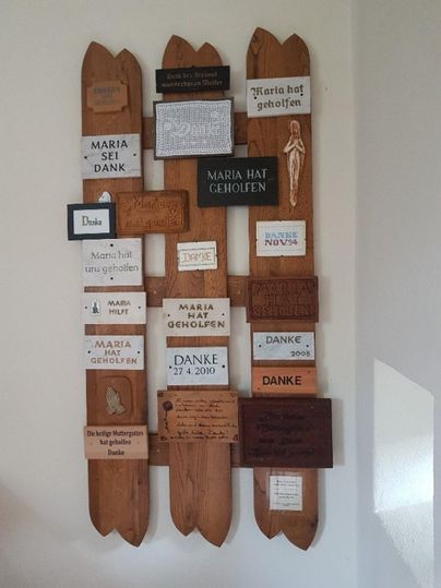 Eine Wandinstallation mit verschiedenen Holztafeln, die Dankesbotschaften und Hinweise enthalten. Die Tafeln sind in unterschiedlichen Formen und Farben gestaltet.