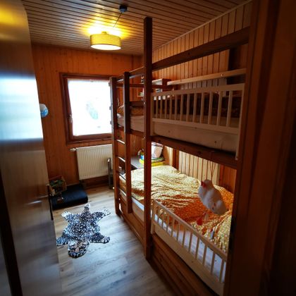 Een gezellige kamer met een stapelbed en kleurrijk beddengoed. De ruimte heeft houten wanden en veel daglicht.