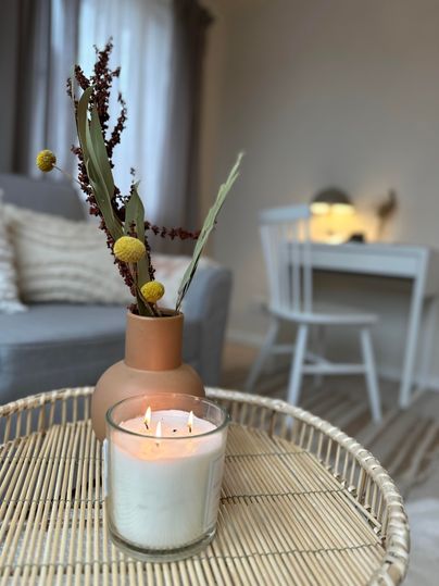 Een gezellige tafel met een kaars en een bloemstuk in een vaas. Op de achtergrond zijn meubels en een neutrale ruimte zichtbaar.